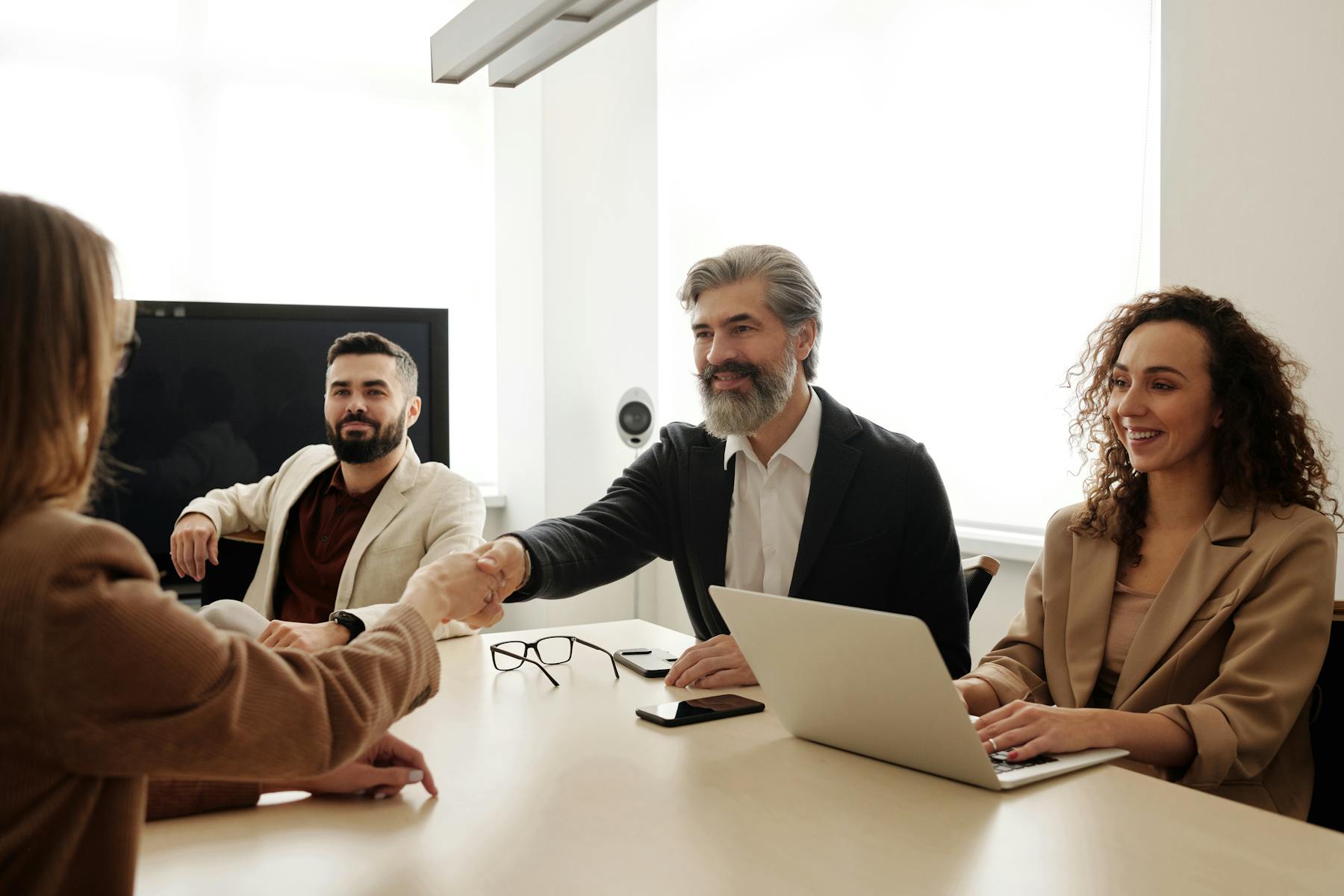 Professionals in blazers and a polo shaking hands during an office meeting